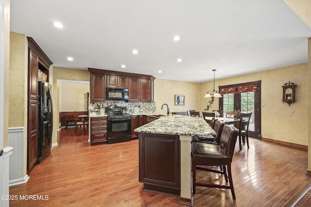 kitchen with black appliances, decorative backsplash, a breakfast bar, light wood-type flooring, and a peninsula