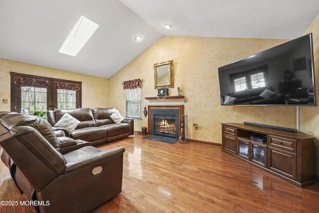 living room featuring a fireplace with flush hearth, baseboards, wood finished floors, and lofted ceiling with skylight