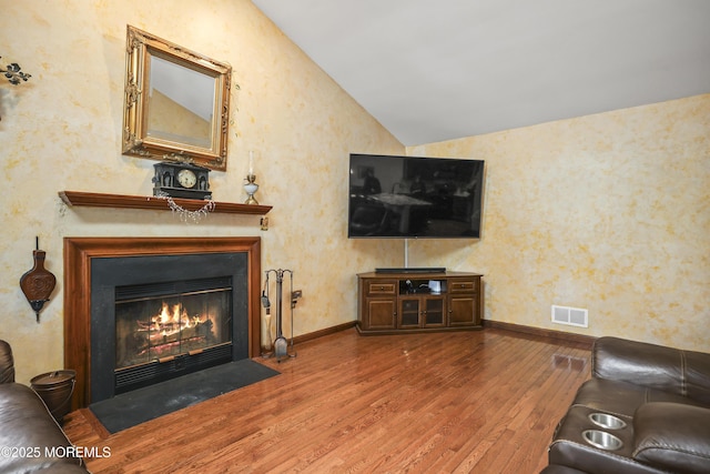 living room featuring wood finished floors, visible vents, lofted ceiling, and baseboards