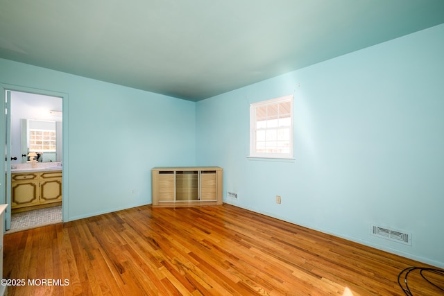 unfurnished bedroom featuring visible vents, connected bathroom, and wood finished floors