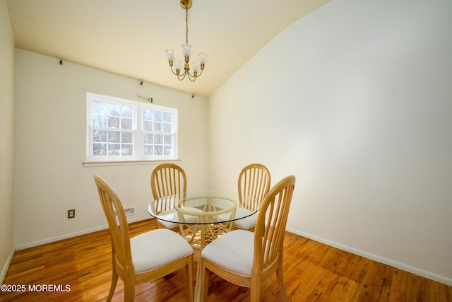 dining space featuring baseboards, wood finished floors, a notable chandelier, and vaulted ceiling