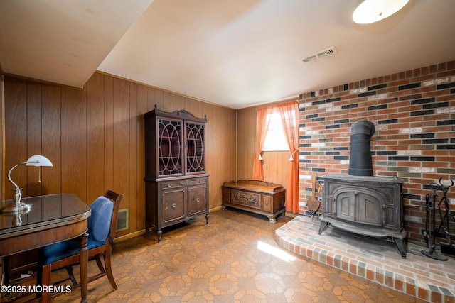 living room featuring wooden walls, visible vents, a wood stove, and tile patterned floors