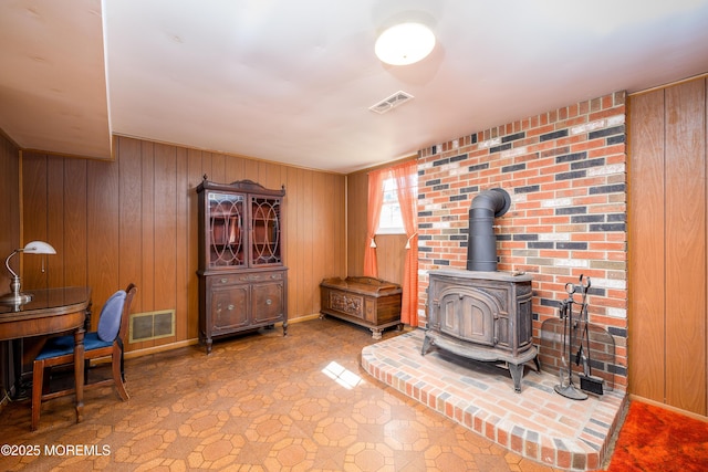 living area featuring a wood stove, wooden walls, and visible vents