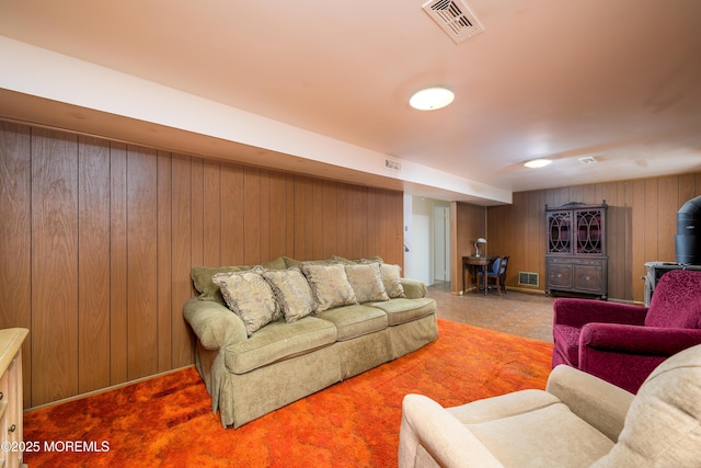 living room featuring wooden walls, visible vents, and a wood stove