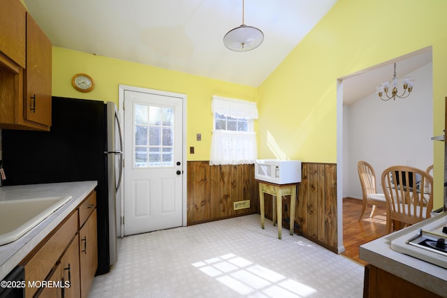 kitchen with white appliances, brown cabinetry, a chandelier, wainscoting, and lofted ceiling