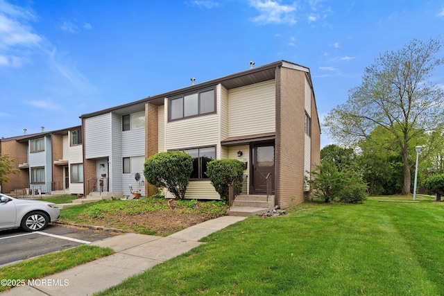 multi unit property with uncovered parking, a front lawn, and brick siding