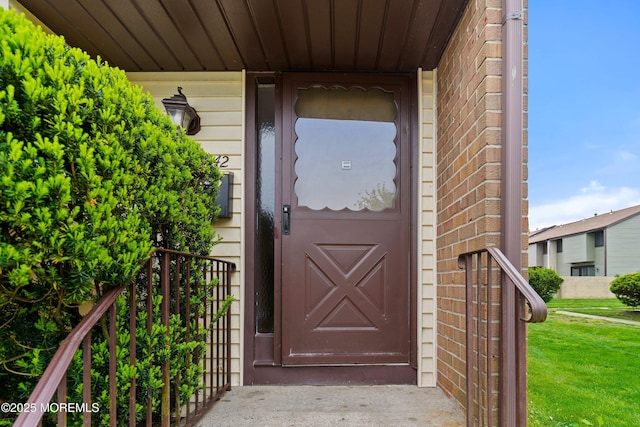 view of exterior entry with brick siding and a lawn