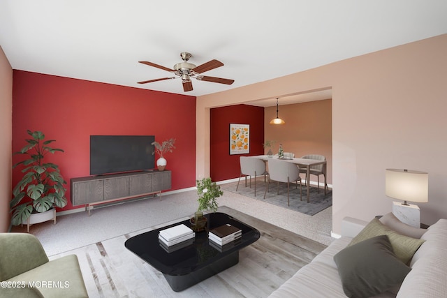 living area featuring ceiling fan, an accent wall, carpet, and baseboards