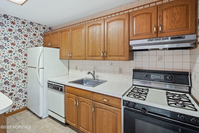 kitchen with wallpapered walls, white appliances, a sink, under cabinet range hood, and light countertops