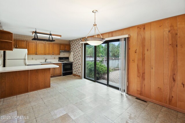 kitchen featuring gas range oven, freestanding refrigerator, a sink, brown cabinets, and light countertops