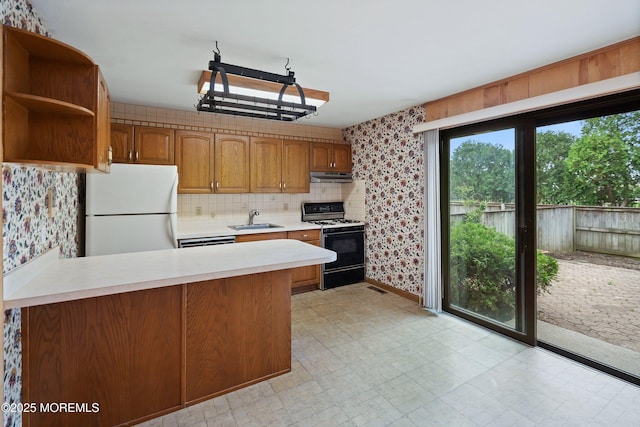 kitchen featuring freestanding refrigerator, gas range, a sink, under cabinet range hood, and light countertops