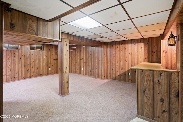 finished basement with carpet, wood walls, and a drop ceiling