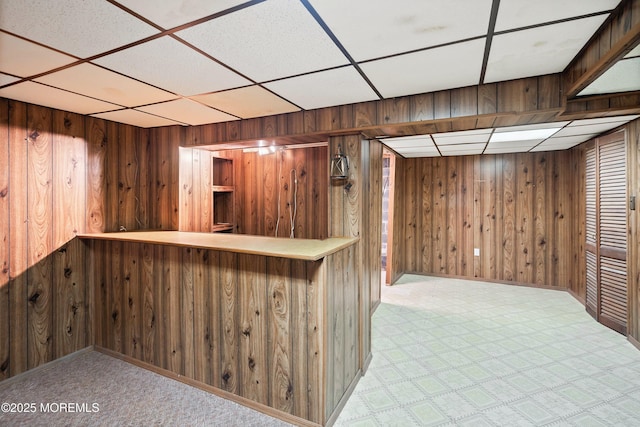 indoor dry bar featuring a paneled ceiling, wooden walls, and baseboards