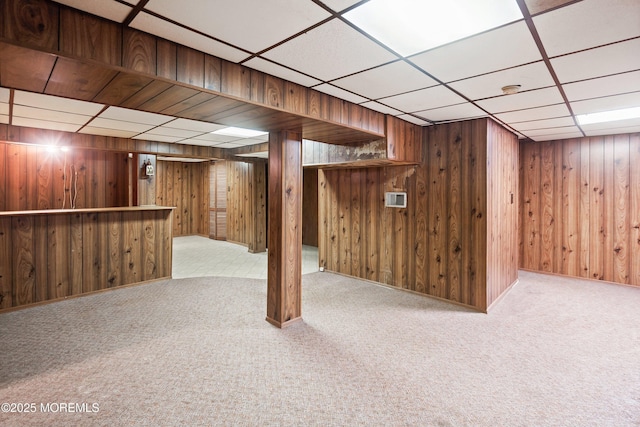 finished below grade area with a drop ceiling, carpet flooring, a bar, and wooden walls