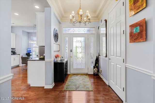 entrance foyer with a chandelier, crown molding, and dark wood finished floors