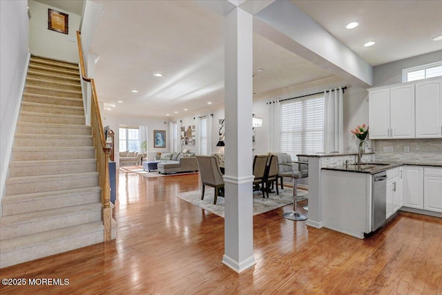 kitchen with plenty of natural light, a sink, light wood-style floors, a peninsula, and white cabinetry