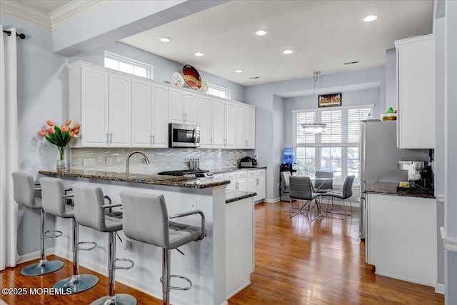 kitchen featuring dark stone countertops, appliances with stainless steel finishes, a peninsula, white cabinetry, and decorative backsplash