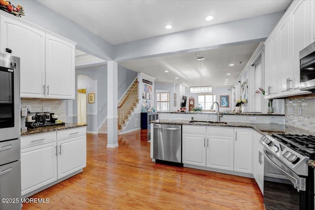 kitchen featuring light wood-type flooring, a peninsula, white cabinets, appliances with stainless steel finishes, and a sink