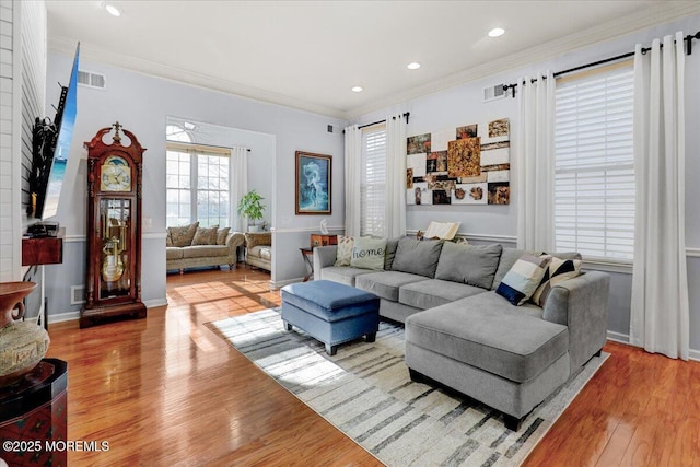 living room featuring visible vents, baseboards, ornamental molding, and wood finished floors