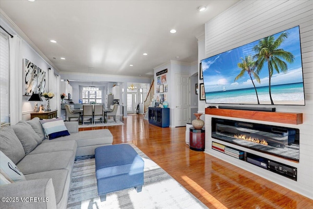 living area with wood finished floors, ornamental molding, a glass covered fireplace, and recessed lighting