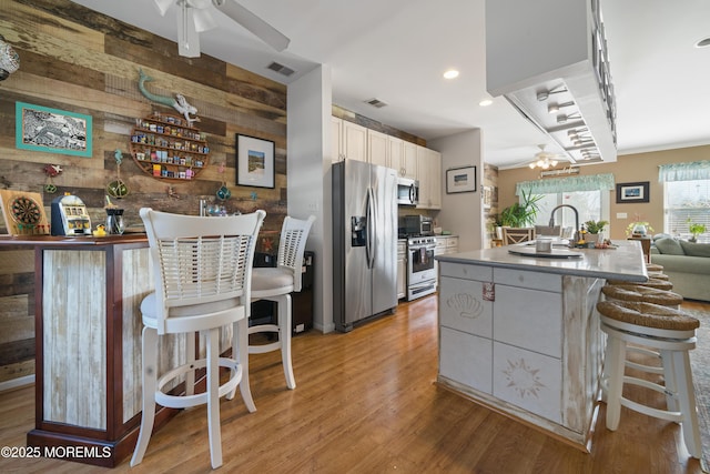33 Blue Heron Ln, Bayville, NJ 08721 - kitchen featuring appliances with stainless steel finishes, wood walls, light wood-style flooring, a ceiling fan, and a kitchen breakfast bar