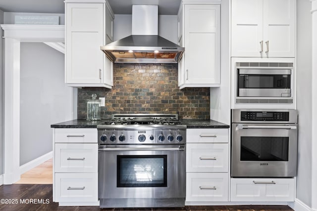 kitchen featuring appliances with stainless steel finishes, wall chimney range hood, backsplash, and baseboards