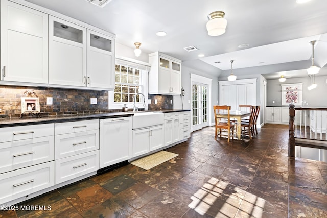 kitchen with visible vents, white dishwasher, a sink, dark countertops, and decorative backsplash