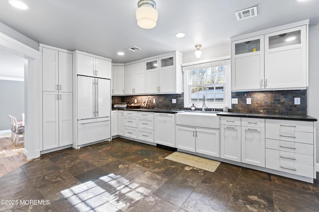 kitchen with built in refrigerator, visible vents, a sink, dark countertops, and white dishwasher