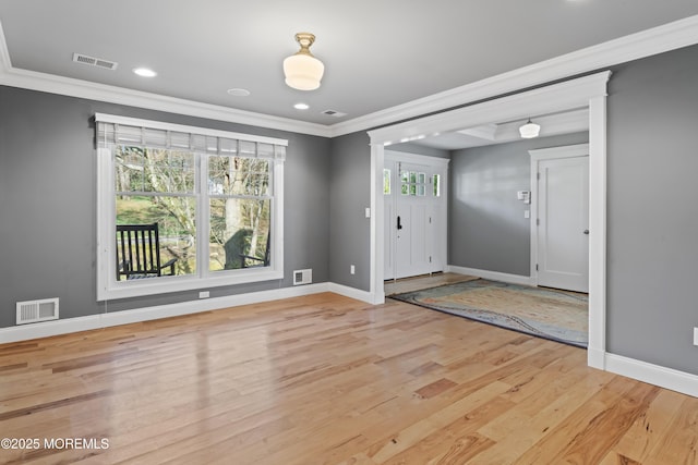 foyer featuring light wood-style floors, baseboards, ornamental molding, and visible vents