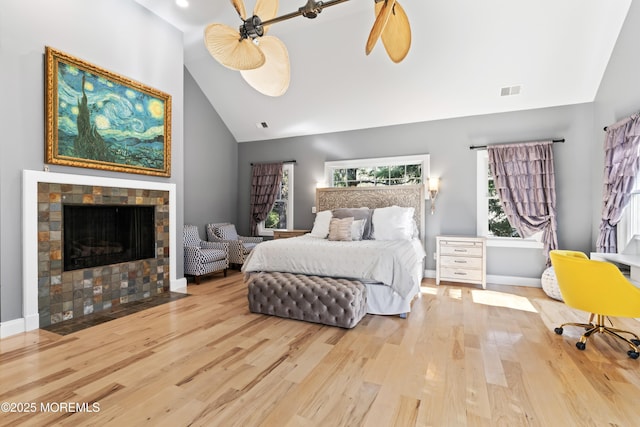 bedroom with baseboards, a fireplace, visible vents, high vaulted ceiling, and wood finished floors