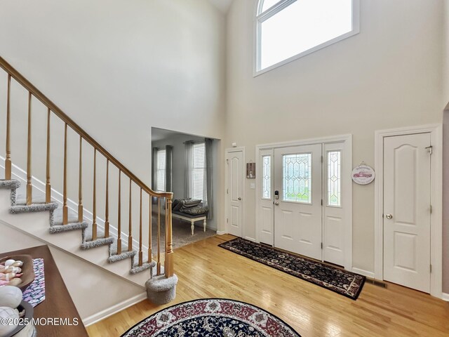 entryway featuring baseboards, a high ceiling, wood finished floors, and stairs