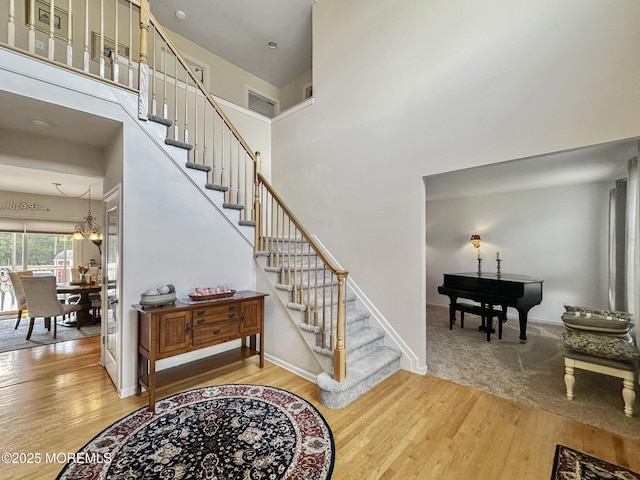 staircase featuring a chandelier, a towering ceiling, baseboards, and wood finished floors