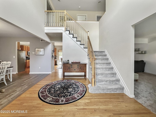 foyer with wood finished floors, a towering ceiling, baseboards, and stairs