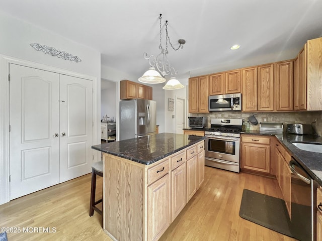 kitchen featuring light wood-style floors, pendant lighting, a center island, appliances with stainless steel finishes, and backsplash