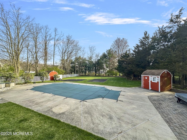 view of pool featuring a shed, a lawn, fence, a patio, and an outbuilding