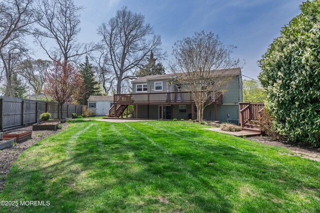 back of property featuring a lawn, a fenced backyard, a wooden deck, a garden, and stairs