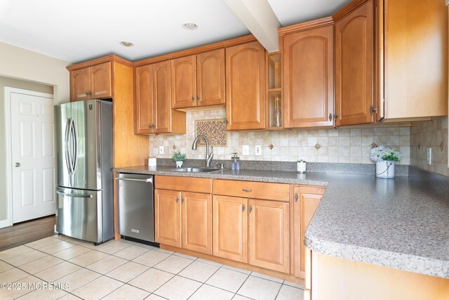 kitchen featuring stainless steel appliances, a sink, backsplash, glass insert cabinets, and brown cabinets