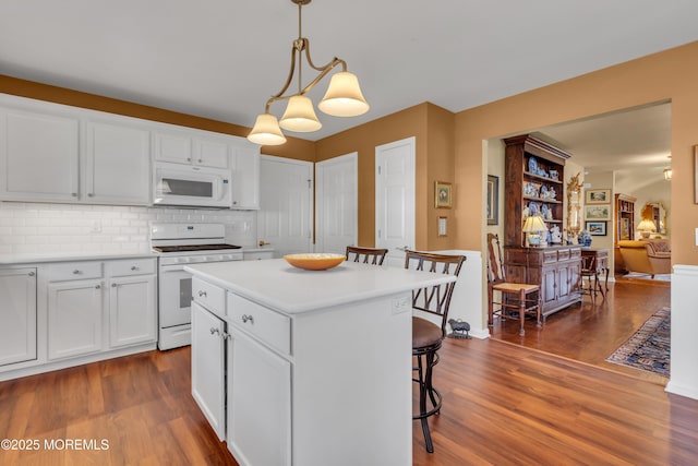 kitchen with a kitchen breakfast bar, tasteful backsplash, white cabinets, dark wood-style floors, and white appliances