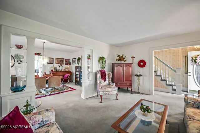 living room featuring carpet floors, stairway, ornate columns, and a notable chandelier