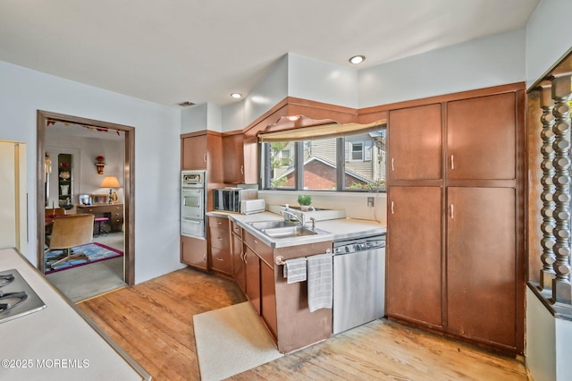 kitchen featuring a sink, light countertops, appliances with stainless steel finishes, brown cabinets, and light wood-style flooring