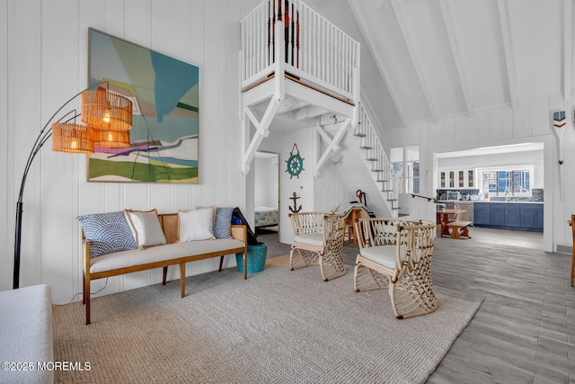living room with wood finished floors, stairs, a decorative wall, beam ceiling, and high vaulted ceiling