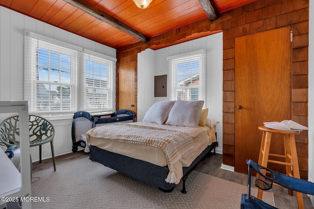 bedroom featuring electric panel, beam ceiling, wood walls, wood finished floors, and wooden ceiling