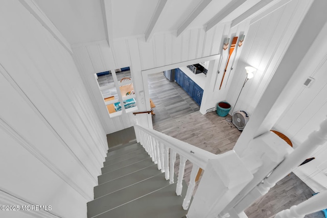 stairway with wood walls, wood finished floors, and beamed ceiling