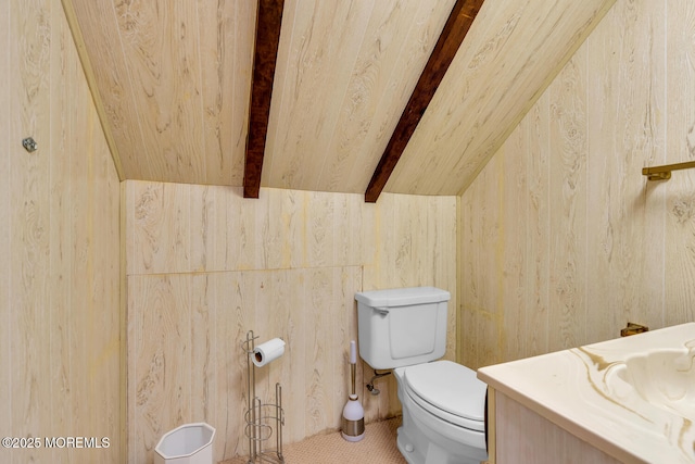 bathroom with lofted ceiling with beams, wood walls, vanity, and toilet