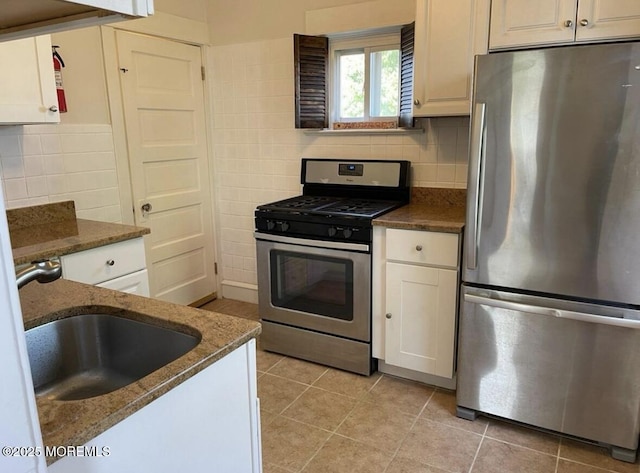 kitchen with decorative backsplash, a sink, light tile patterned floors, dark stone countertops, and stainless steel appliances