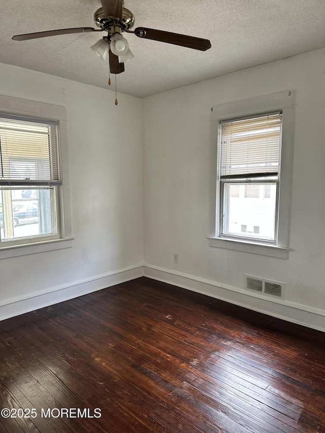 unfurnished room featuring visible vents, dark wood-type flooring, and a wealth of natural light