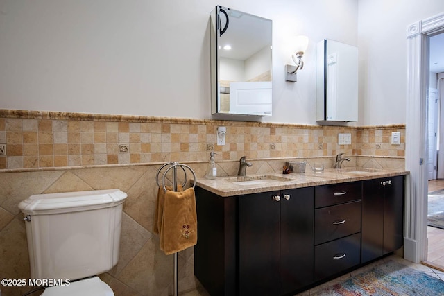 full bathroom featuring a sink, tile walls, toilet, and double vanity