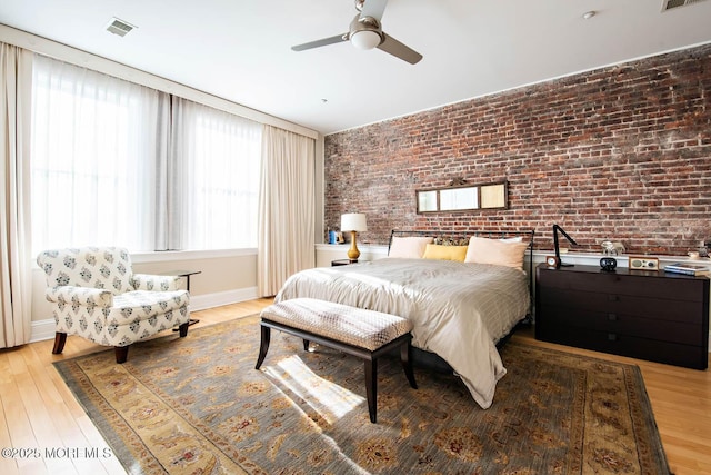 bedroom with visible vents, baseboards, light wood-style floors, and brick wall