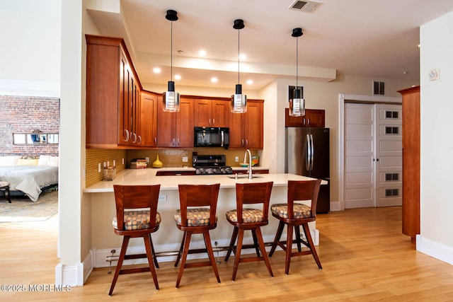 kitchen with a sink, freestanding refrigerator, a peninsula, black microwave, and stove