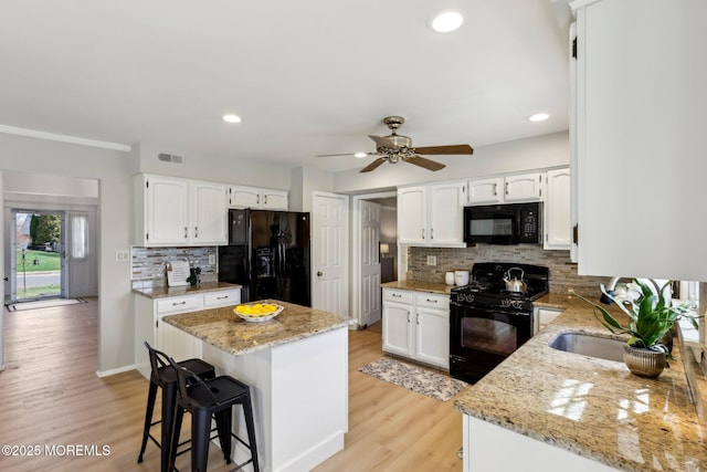 kitchen featuring visible vents, light wood-style flooring, black appliances, and light stone countertops